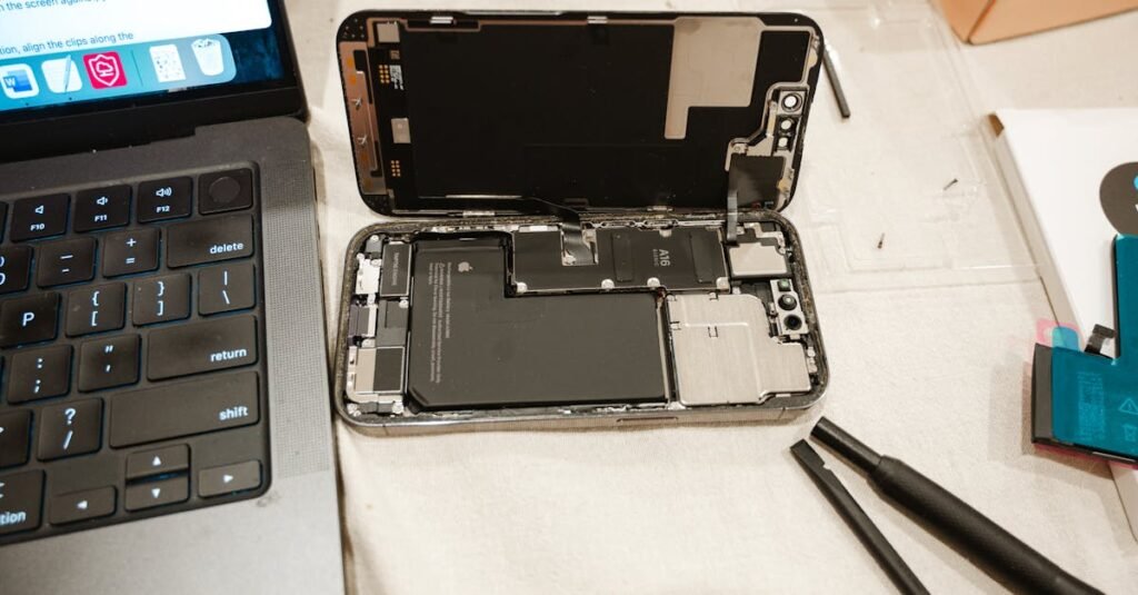 Open iPhone with repair tools and laptop, showcasing DIY battery replacement process.