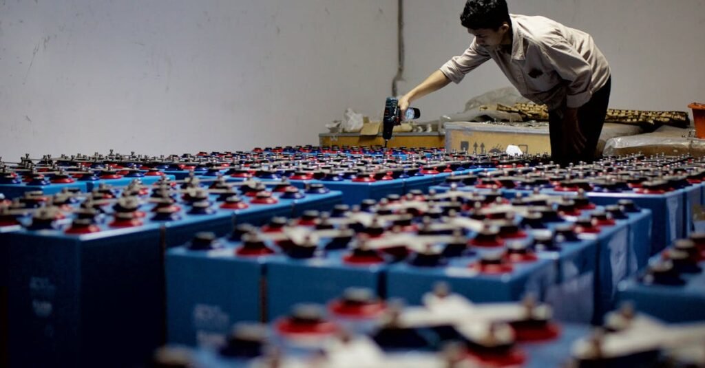 A worker checking many industrial batteries inside a facility. Indoor, industrial setting.
