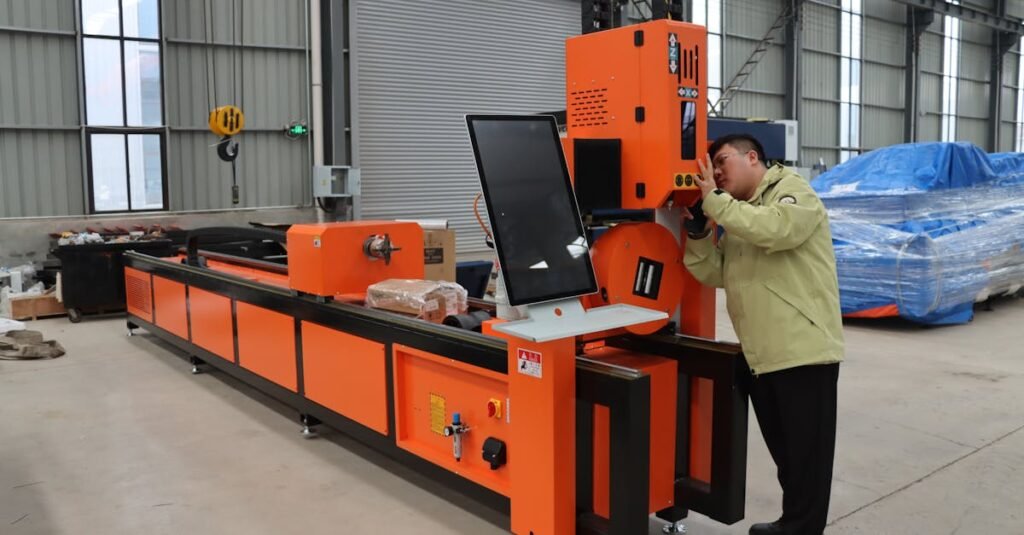 Engineer adjusting an orange CNC machine in a large industrial warehouse setting.