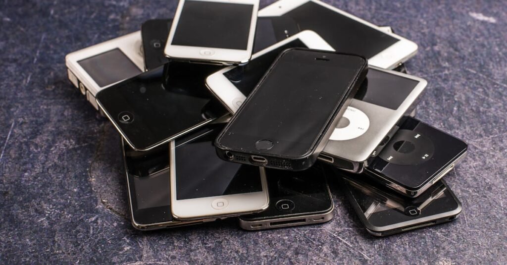 Stack of assorted aged cellphones with black screens and portable music players on gray background