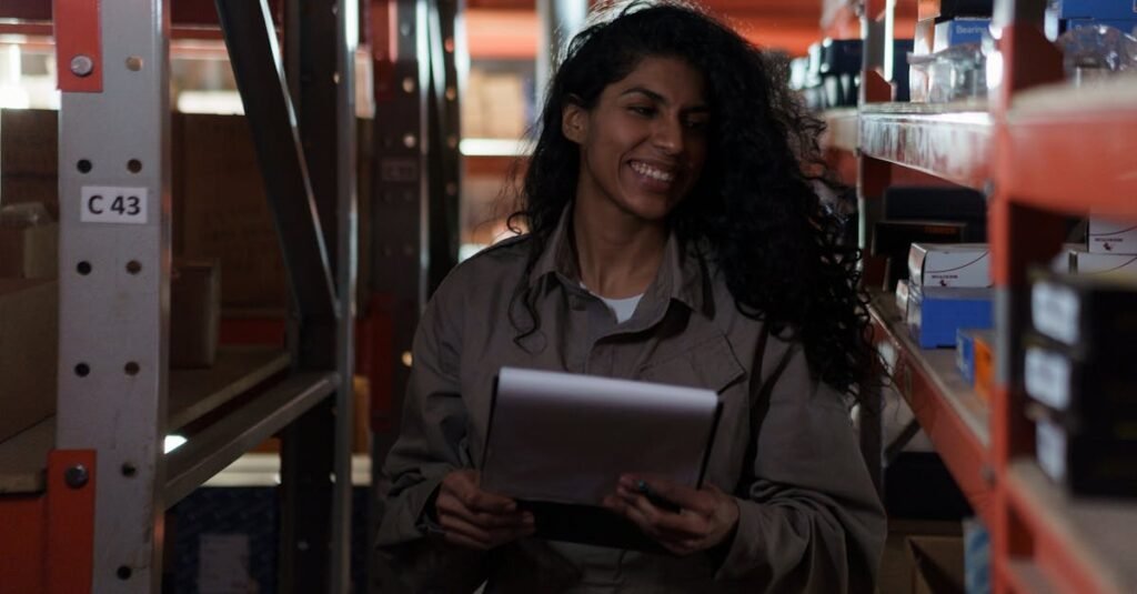 Woman managing inventory with clipboard, smiling in a dimly lit warehouse aisle.