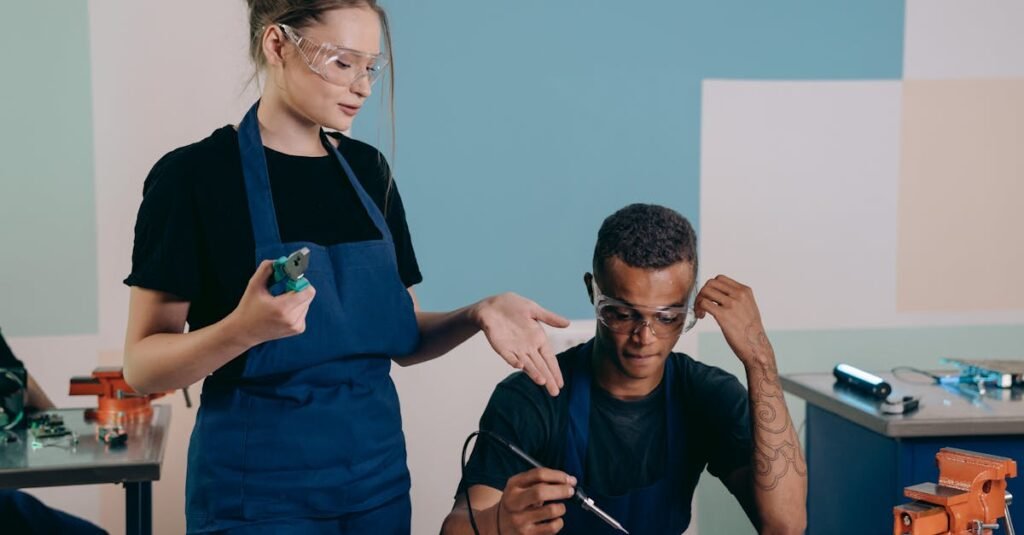Two technicians working together on electronics with safety gear in a workshop.