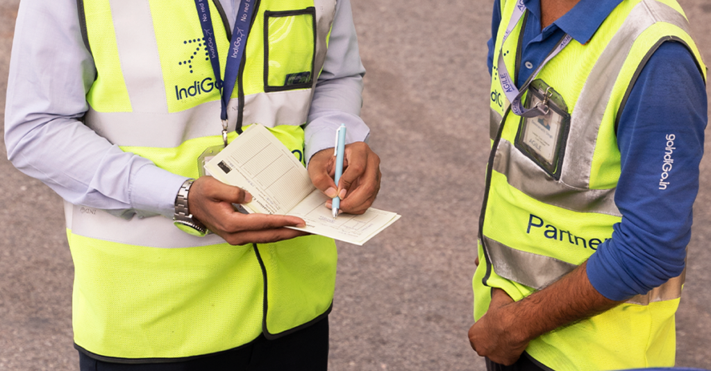 Two airport staff in high-visibility vests reviewing documents while wearing face masks.