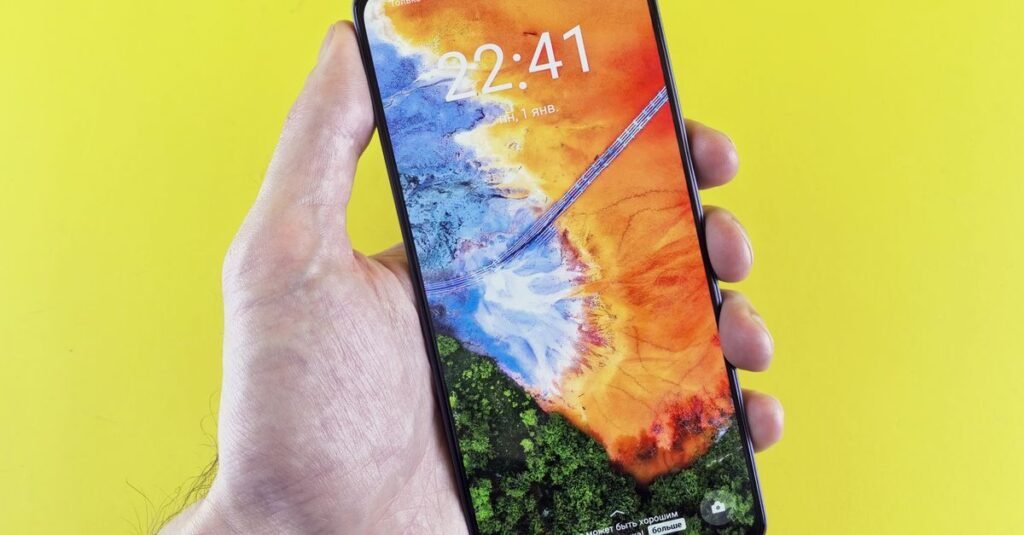 Close-up of a hand holding a smartphone with vivid colors on its screen, set against a yellow background.