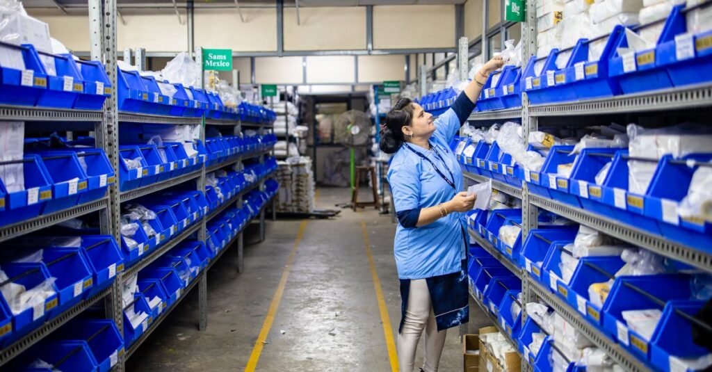 Woman in uniform organizing inventory in a warehouse aisle with labeled bins.
