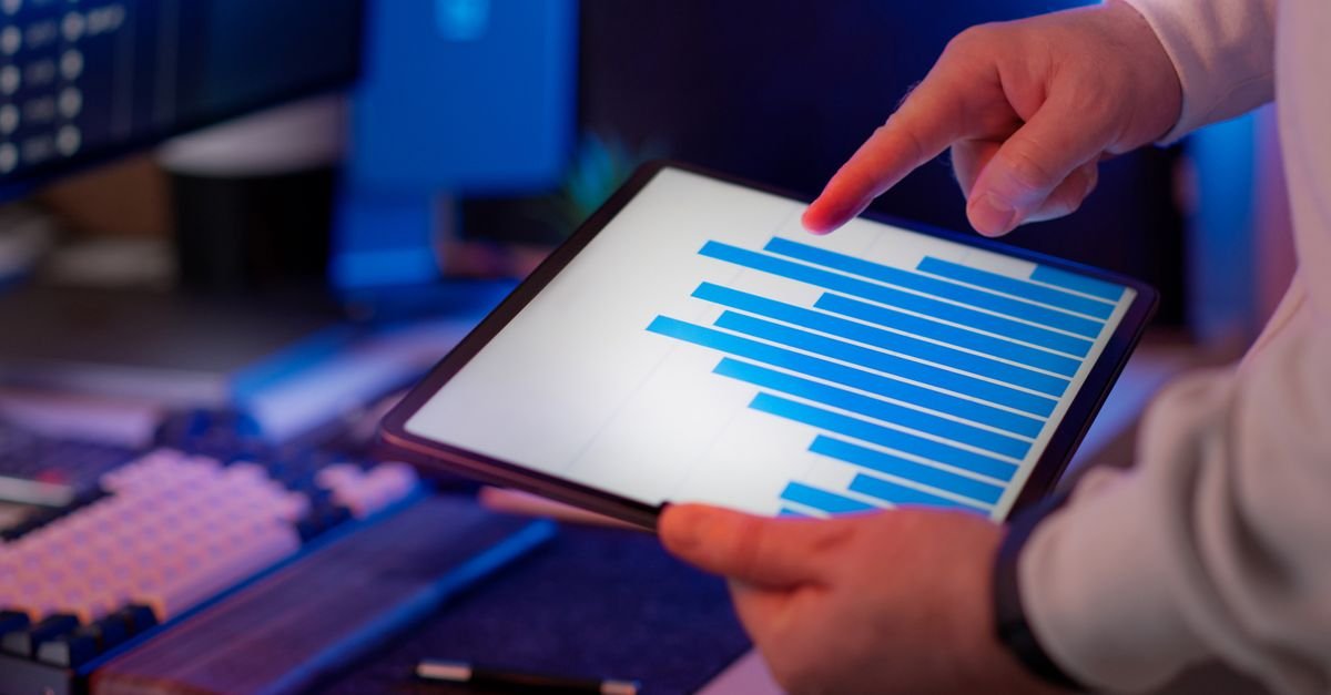 Business professional analyzing bar chart on tablet in office setting, highlighting data insights.