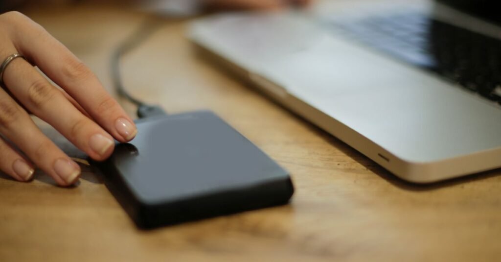 Close-up of a person connecting an external hard drive to a laptop on a desk.