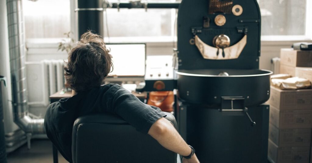 Man observes coffee roasting process in industrial setting with modern equipment.