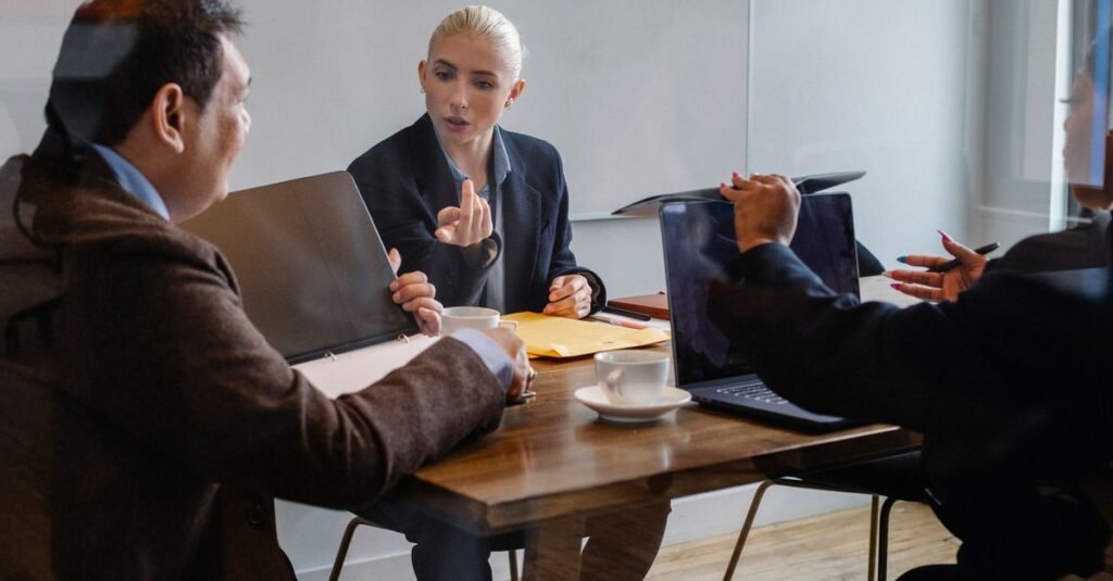 Group of diverse coworkers in formal wear gathering around table with laptop and documents during business meeting