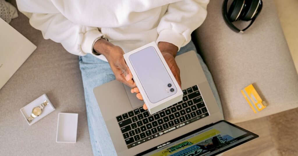 Person unboxing a new smartphone while sitting with a laptop, ready for online shopping on a cozy sofa.