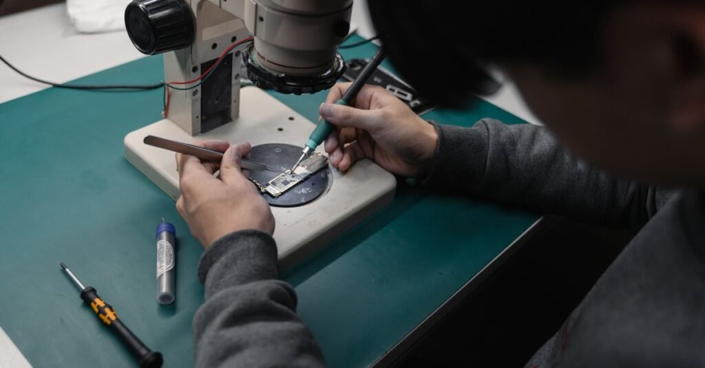 Technician using a microscope to repair a broken electronic board with precision tools.
