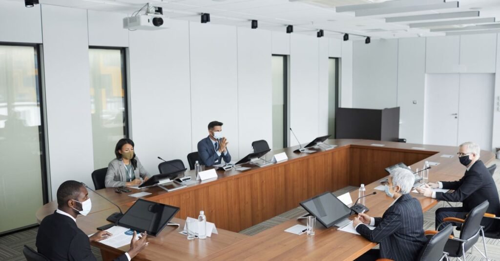 Business professionals wearing masks attending a conference meeting in a modern setting.