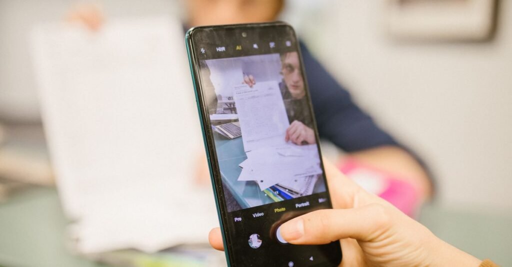 Close-up of student using smartphone to photograph examination papers in a classroom setting.