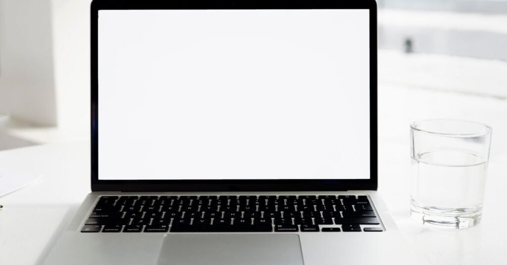 A sleek laptop on a white desk with a glass of water, offering a clean and minimalist workspace.