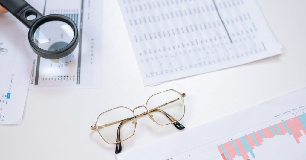 Flat lay of business documents with magnifying glass, glasses, and smartphone on a desk.