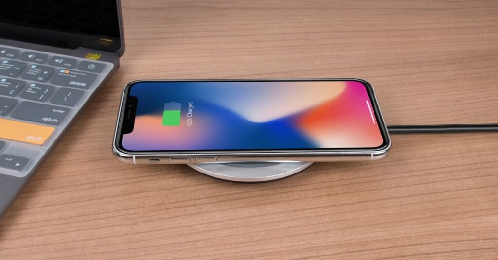 Mobile phone charging wirelessly on a desk next to a laptop, showcasing modern technology.
