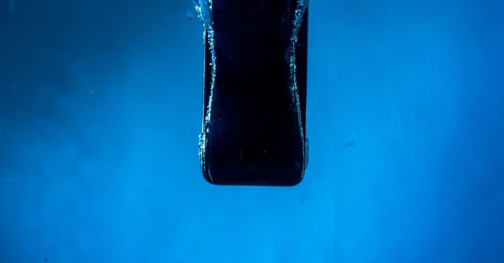 A smartphone partially submerged in water, captured against a blue backdrop.