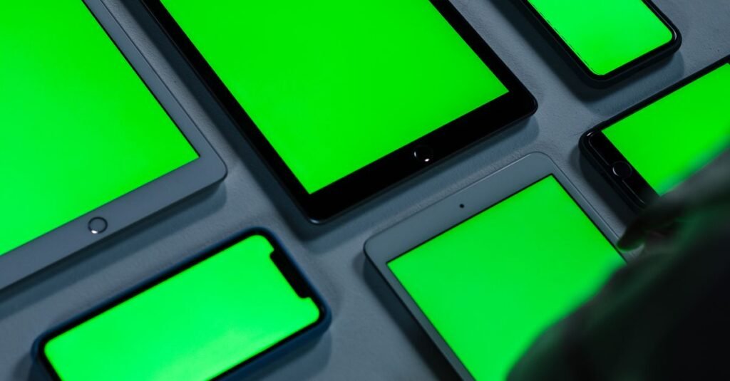 A variety of digital devices with green screens arranged on a table indoors.